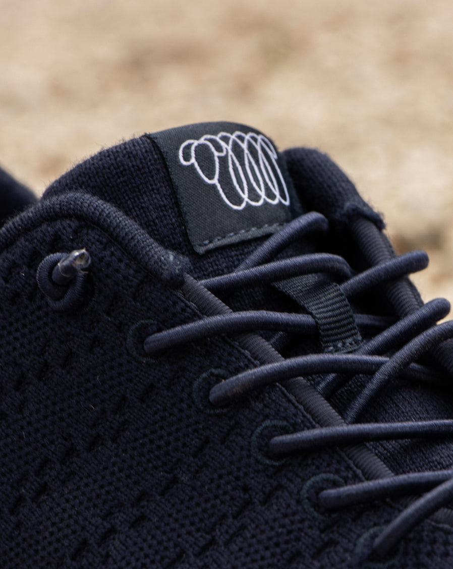 Close-up of navy blue Woolloomooloo sneaker showing the laces, knit texture, and brand logo on the tongue