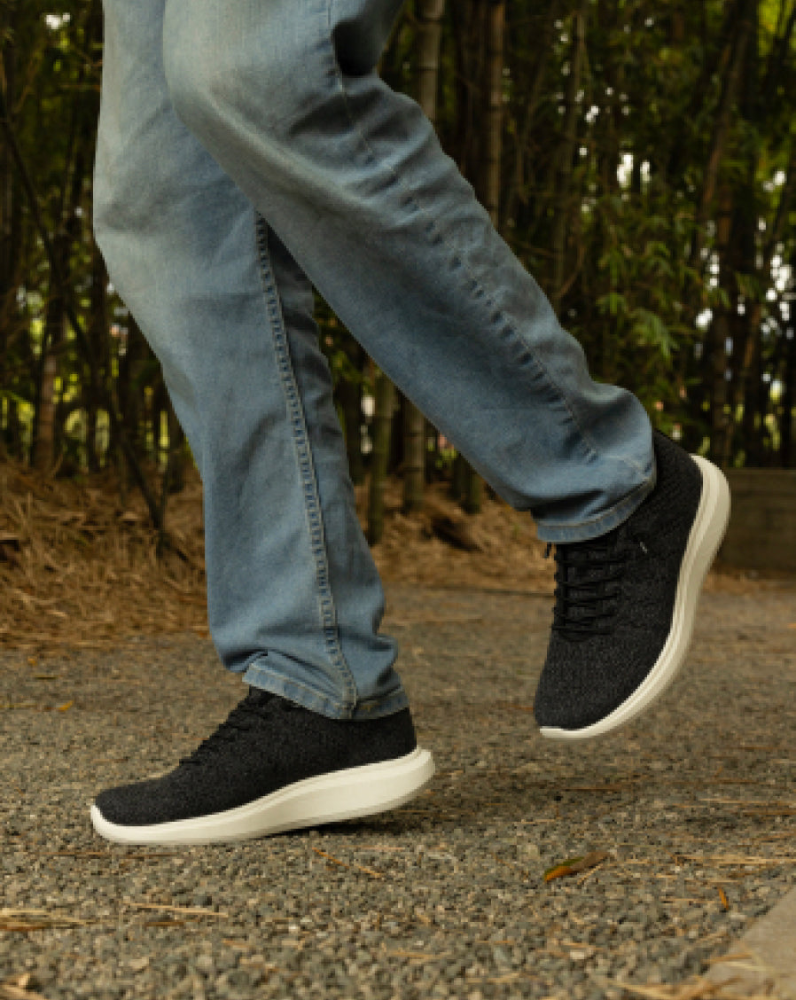 Close-up of person wearing navy blue Woolloomooloo sneakers with white soles, standing on a gravel surface in light blue jeans